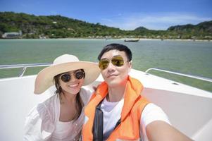 emocionada pareja de turistas tomándose un selfie en una lancha rápida con una hermosa vista del océano y la montaña en el fondo foto