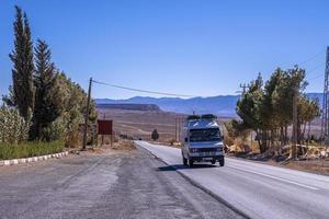 Van travelling on rural road by deserted land against blue sky photo