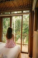 A woman wears a dress and sit the middle of bedroom and window. photo