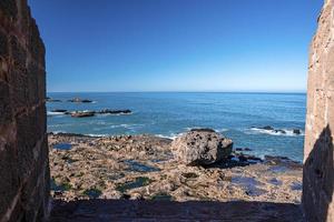 Stone walls with rocky sea coastline against clear blue sky