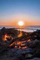 hoguera con leña ardiendo durante la hermosa puesta de sol en la playa foto