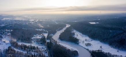 vista aérea del río y del bosque cubierto de nieve después de una ventisca en una neblina matutina. cielo azul claro. las maravillas de invierno. parque nacional de gauja, sigulda, letonia foto