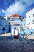 Public drinking water fountain outlet amidst traditional old blue colored facade of houses photo