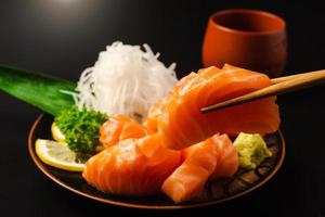 sashimi, salmón, palillos de comida japonesa y wasabi con plato negro foto