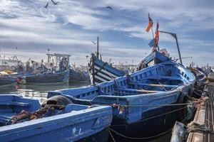 Barcos de pesca azules de madera anclados en el puerto deportivo contra el cielo nublado foto