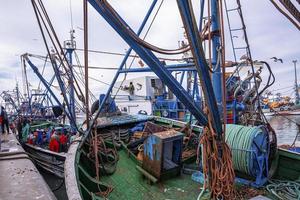 Wooden fishing boats anchored beside pier at marina against cloudy sky photo