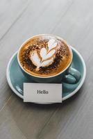 Cup of coffee with latte art and Hello greeting text on wood table photo