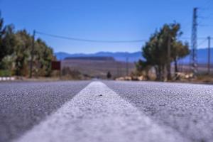 Straight asphalt road with white surface marking against mountains in background photo