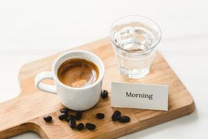 Fresh cup of brewed espresso coffee shot served for breakfast on wooden platter with good morning greeting card photo