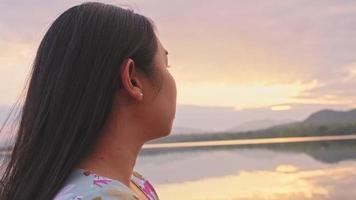 jovem turista feminina à beira do lago apreciando a bela vista da natureza ao pôr do sol. conceitos de estilo de vida e turismo ao ar livre. video