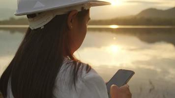 Female engineer working with a smartphone at the dam construction site to generate electricity. Confident woman architect in white helmet looking at a dam construction site. video