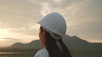 la ingeniera examina el sitio de construcción de la presa para generar electricidad. mujer arquitecta segura de sí misma con casco blanco mirando el sitio de construcción de una presa. conceptos de tecnología y energía limpia. video