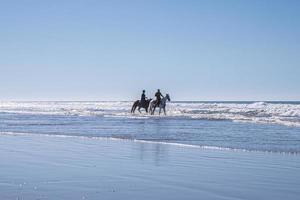 Man and woman riding horses along shoreline at beach against clear sky photo