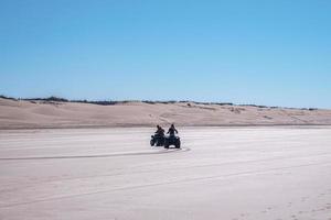 People riding quad bikes through sandy road along with sand dunes photo