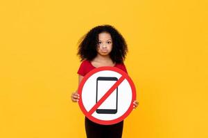 Mixed race African girl showing no mobile phone usage sign isolated on colorful yellow background