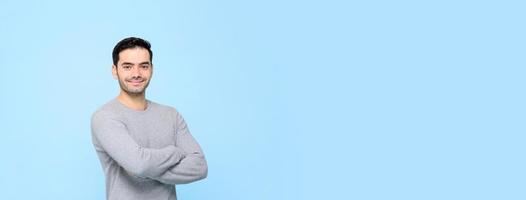 retrato de un hombre guapo y sonriente con una camiseta gris con los brazos cruzados aislado en un fondo de pancarta azul claro con espacio para copiar foto