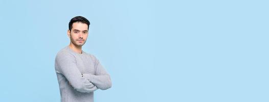 Confident handsome man in casual gray t-shirt doing arm crossed gesture isolated on light blue banner background with copy space photo