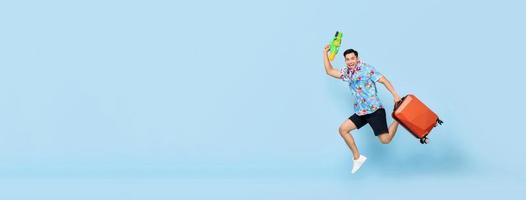 Jumping handsome Asian tourist man traveling with water gun and baggage during Songkran festival on banner blue background with copy space