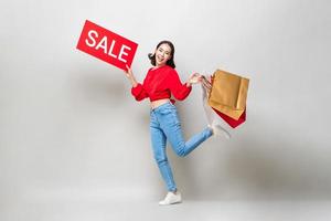 Surprised Asian woman holding shopping bags and red sale sign isolated in gray studio background for Chinese new year sale concept photo
