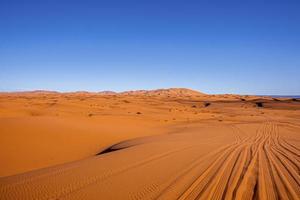 Amazing view of sand dunes with tyre marks  in desert against clear sky photo