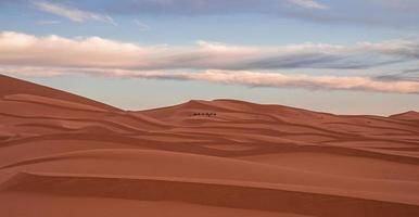 Amazing view of sand dunes with waves pattern in desert against cloudy sky photo