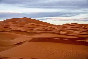 Impresionante vista de las dunas de arena con patrón de ondas en el desierto contra el cielo nublado foto