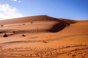 Sand dunes with tyre marks  in desert on sunny summer day against sky photo