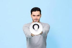 joven apuesto hombre con megáfono aislado sobre fondo azul claro foto