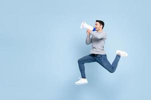 Young active man jumping and shouting on megaphone isolated on light blue background with copy space photo