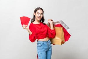 sonriente mujer asiática feliz sosteniendo bolsas de compras y sobres rojos aislados en un fondo de estudio gris claro para el concepto de venta de año nuevo chino