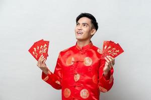 Asian man in traditional oriental costume holding red envelopes or Ang Pao with text mean lucky - wealthy for Chinese new year concepts photo