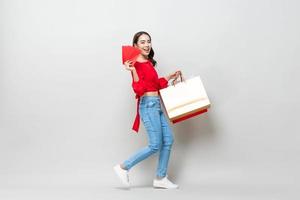 mujer asiática feliz sosteniendo bolsas de compras y sobres rojos o ang pao aislado en fondo de estudio gris claro para el concepto de venta de año nuevo chino
