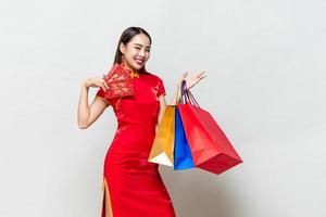 Asian woman in traditional dress holding bags and red envelopes in isolated light gray studio background for Chinese new year shopping concept, text means great luck great profit photo