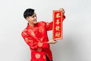 un apuesto hombre asiático sonriente que muestra una etiqueta roja en un estudio aislado de fondo gris claro para los conceptos del año nuevo chino, el texto significa que puede obtener una mayor riqueza
