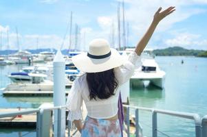 turista emocionado con sombrero blanco disfrutando y parado en el muelle con yates de lujo durante el verano foto