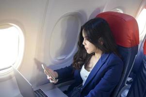 una joven empresaria vestida con traje azul está usando una computadora portátil a bordo