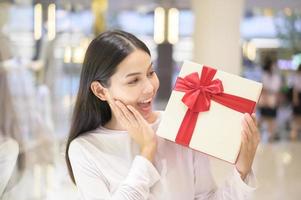 mujer sosteniendo una caja de regalo en el centro comercial, acción de gracias y concepto de navidad. foto