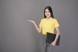 young confident beautiful woman wearing yellow shirt is holding documents on grey background studio photo