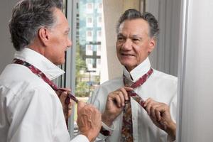 Mature Business Man Tying his Neck Tie in Front of a Mirror photo