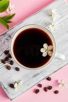 Cup of strong espresso coffee and delicate spring flowers on a pink background. photo