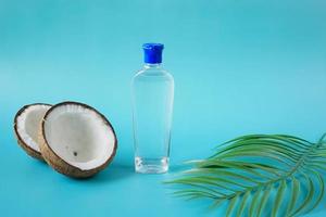 slice of fresh coconut and bottle of oil on blue background photo