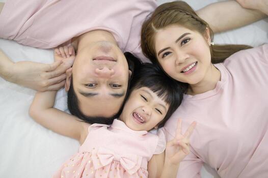 Top view of a happy asian family wearing pink shirt portrait on white bed indoor photo
