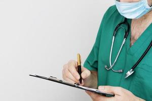 A doctor in uniform, a mask with a stethoscope, writes on a writing board with a pen. Medical concept. Copy space for text photo