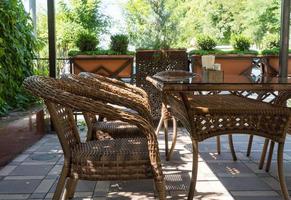 tables and wicker chairs in outdoor summer cafe with flower beds