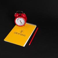 alarm clock with notepad and colored pencils on black background, isolated. back to school. great ideas photo
