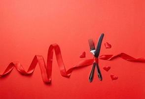 Fork and knife tied with a red ribbon in a shape of heart rate on red background photo