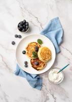 Cottage cheese pancakes served with curd and blueberries, top view flat lay on marble background