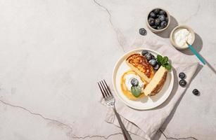 Cottage cheese pancakes served with curd and blueberries, top view flat lay on concrete background, copy space