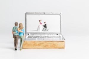 Miniature people Bride and groom virtual wedding on computer screen photo