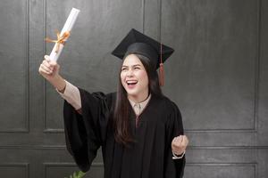 Portrait of young woman in graduation gown smiling and cheering on black background photo